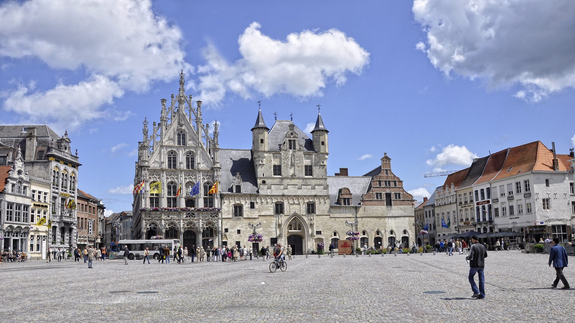 L’hôtel de ville de Malines sur la Grand-Place, avec sa façade gothique à balcon et ses deux tourelles, sous un ciel bleu nuageux