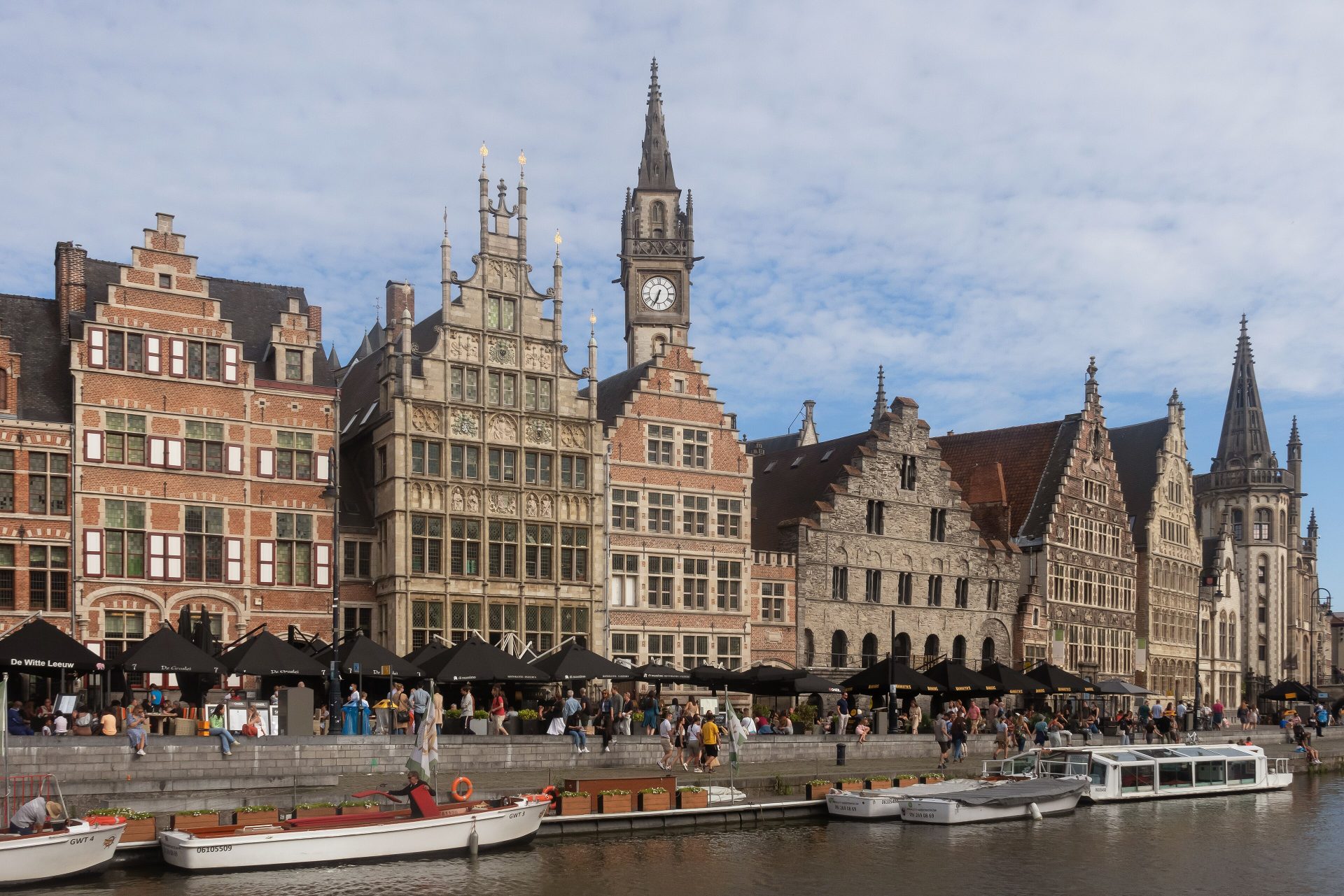 De gildehuizen aan de Graslei in Gent, gezien over de Leie vanaf de Korenlei, met de klokkentoren van het oude postgebouw erachter en bootjes aan de kade