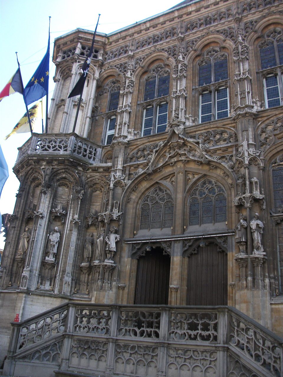 De rijk versierde gotische gevel van het stadhuis van Gent, met beelden in nissen, een stenen buitentrap en vlaggen aan de hoektoren