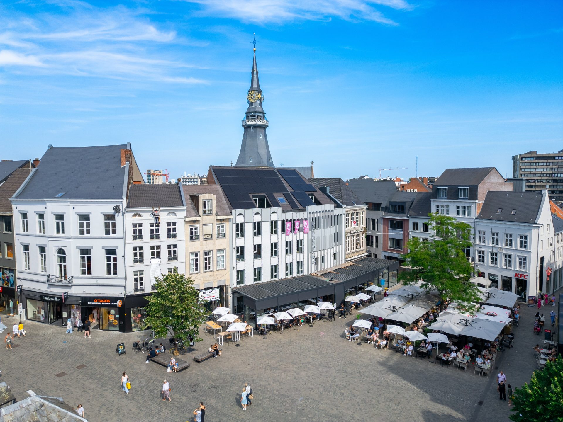 La Grote Markt de Hasselt vue d’en haut, avec des terrasses sur la place, des façades blanches et, derrière elles, la flèche de la cathédrale Saint-Quentin
